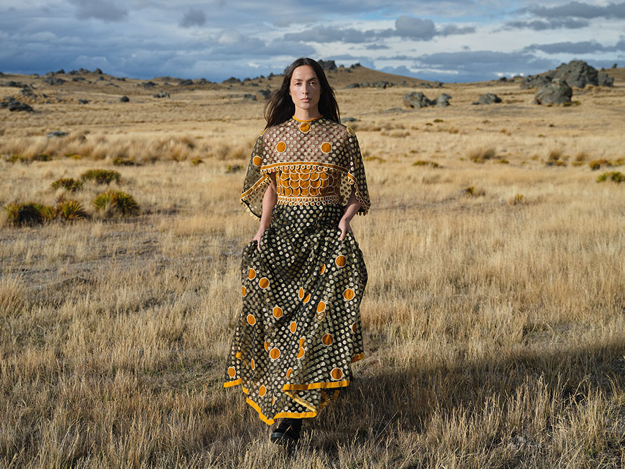 Kevin Berkahn evening dress, early 1970s. Nylon net, Lurex and cotton velvet dots, EH17. Photographed at Poolburn Reservoir, 2024. Model: Ngahuia Williams. Image supplied by Te Papa Press/Eden Hore Central Otago. Image © Derek Henderson. WORD CHCH 2025 04